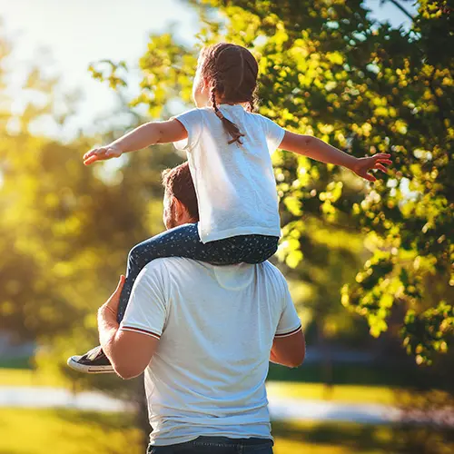 Daughter sitting on her father's shoulders walking in the park