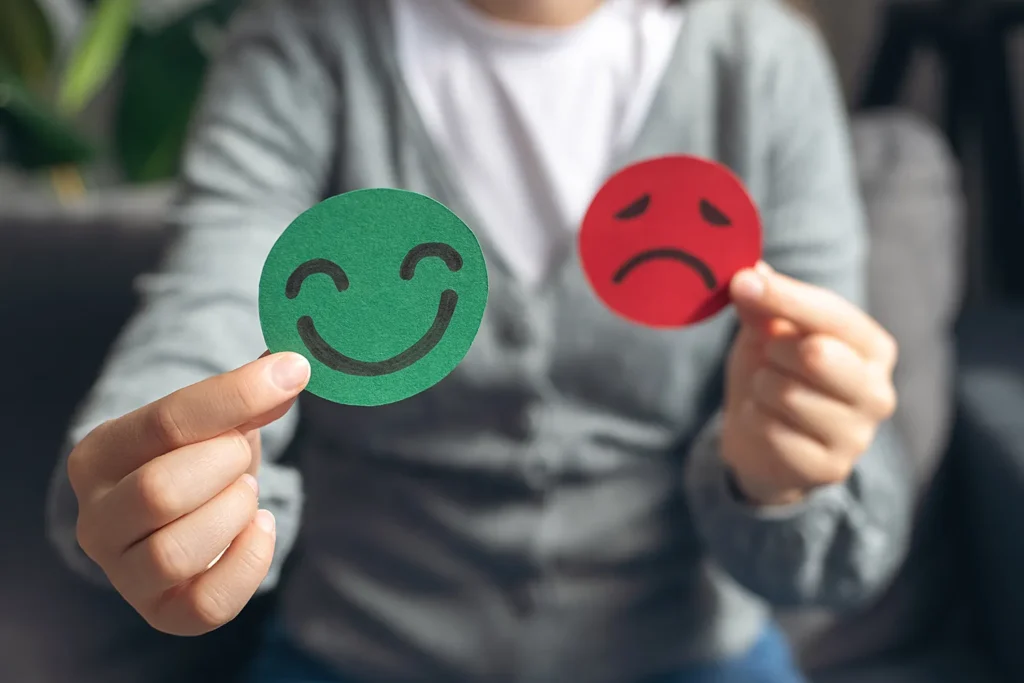Close-up of a person holding a green happy face and a red sad face cutout, representing different emotional states.