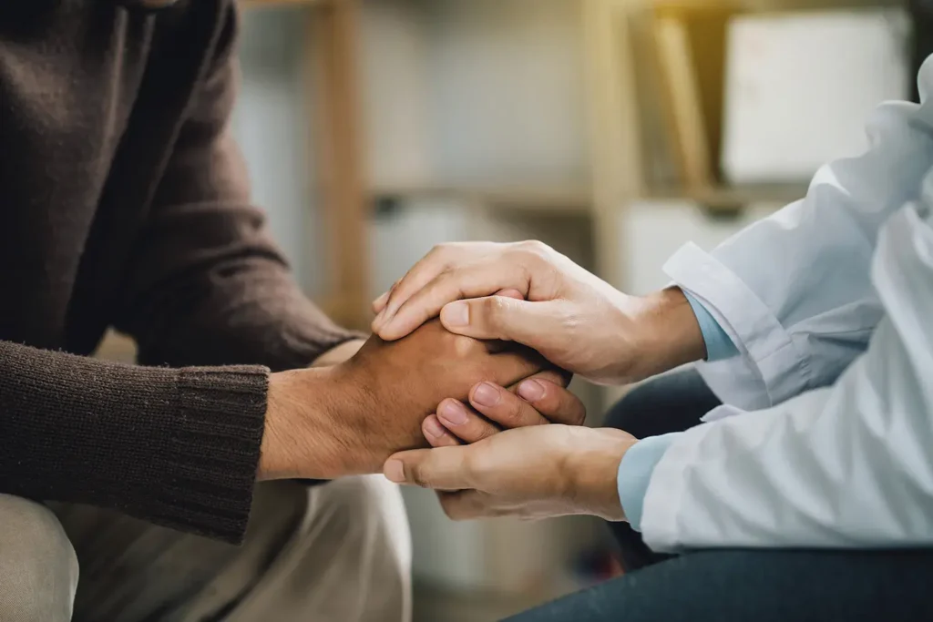 Doctor holding and comforting a patient’s hands during a supportive conversation.