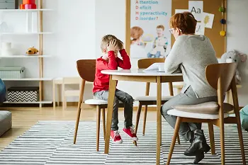 A child struggling with ADHD sits with a teacher in the classroom
