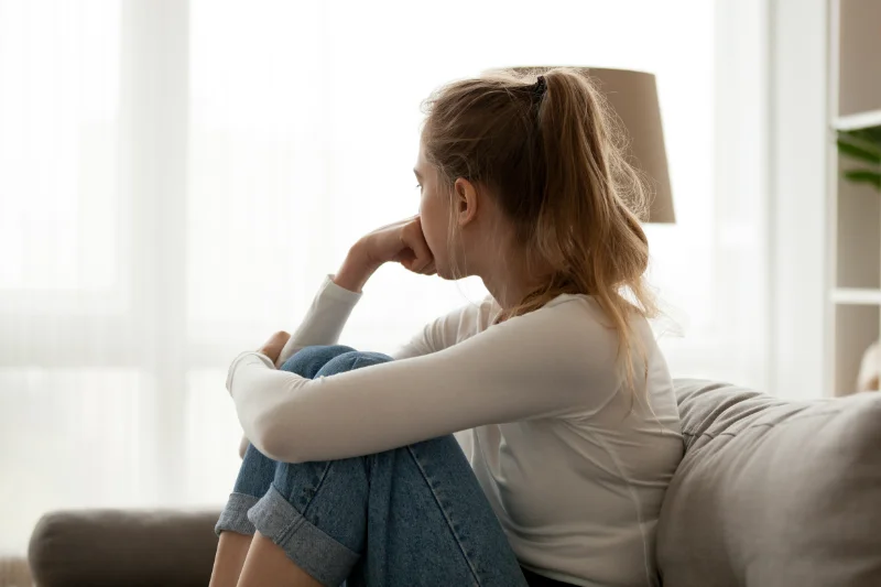 A woman sitting on a couch looking away with her hand on her face