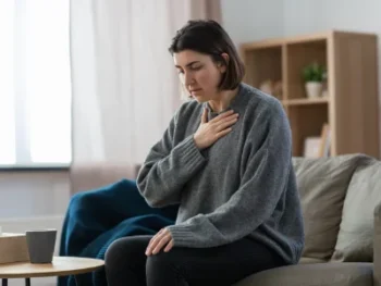 Distraught woman sitting on couch with hand on chest.